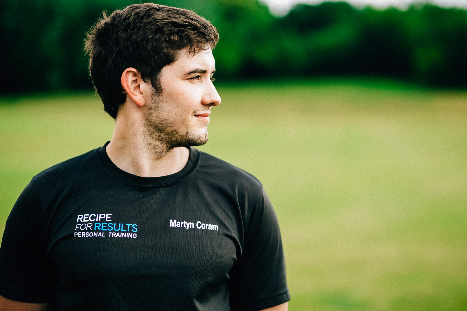 Personal trainer wearing a Recipe For Results T-shirt looking to the side outdoors.