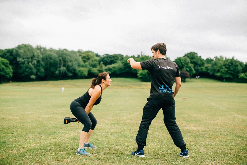 Outdoor personal training session in Essex with a client performing kettlebell swings while the trainer provides guidance and motivation.